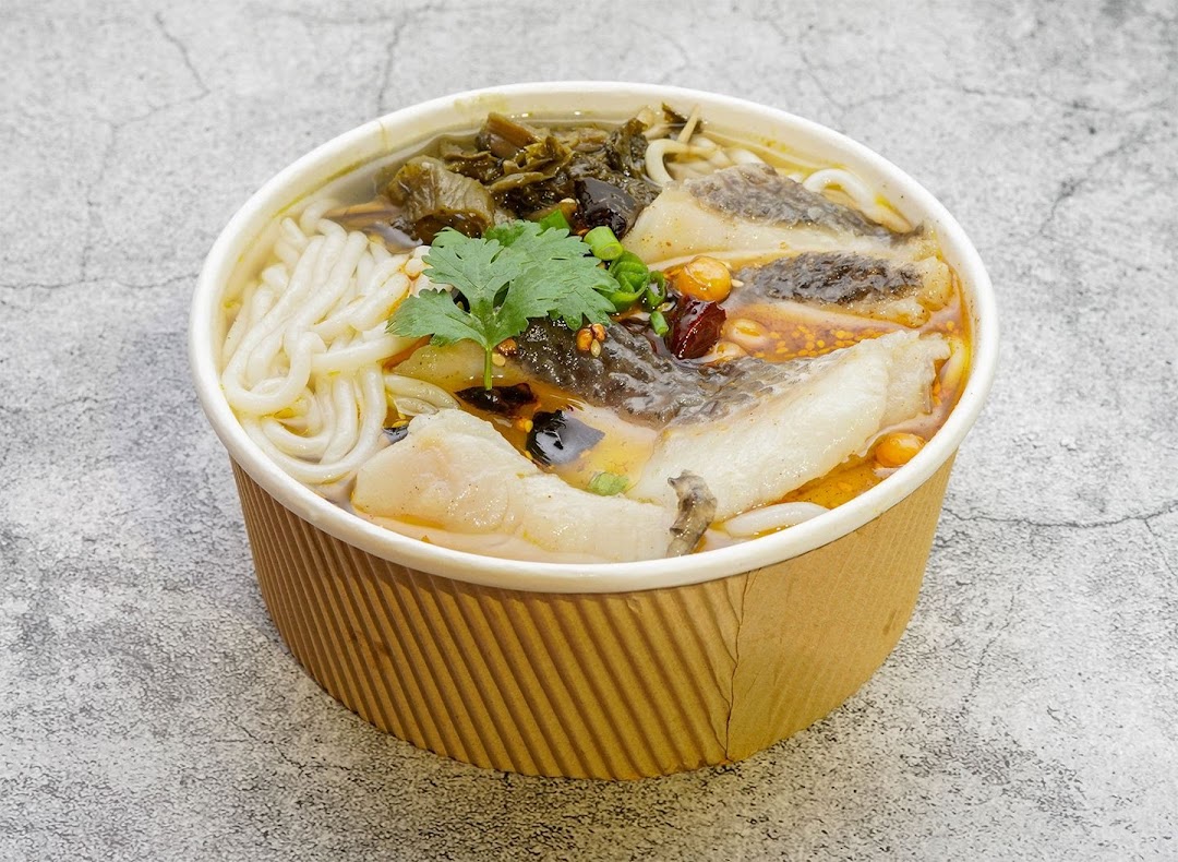 A close-up of a delicious bowl of noodles with fish fillets, pickled vegetables, and cilantro.