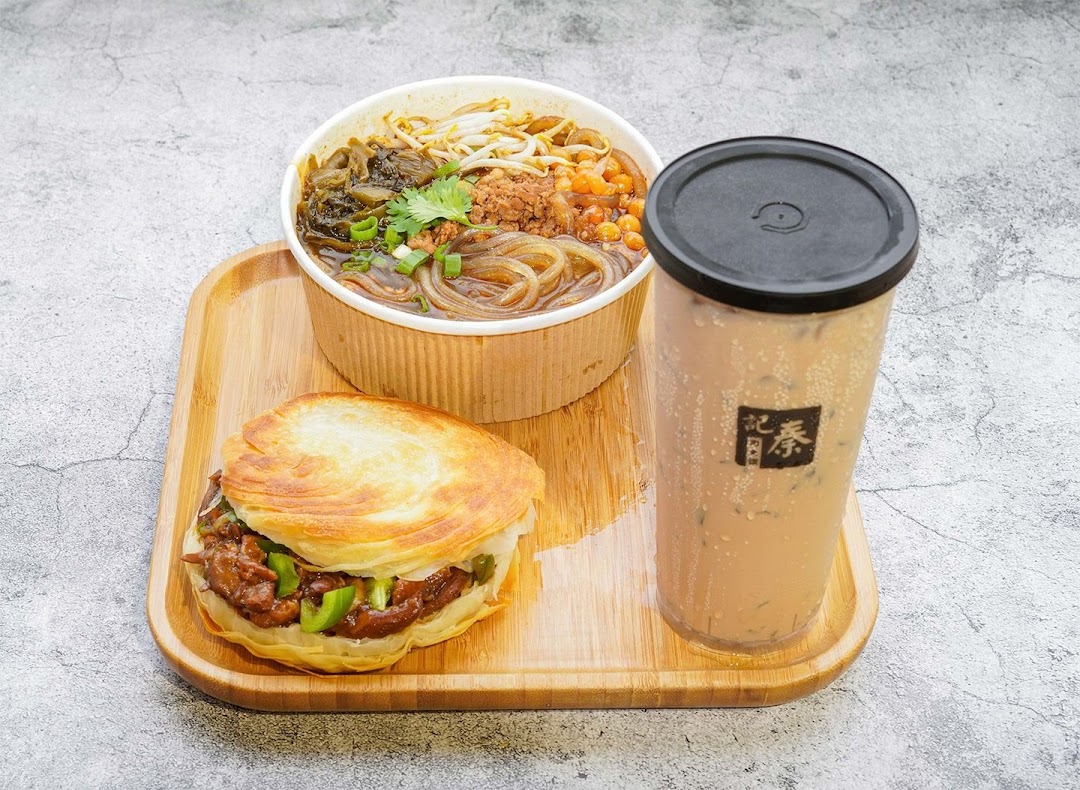 A delicious meal set featuring a rougamo, a noodle soup, and a refreshing beverage on a wooden tray.