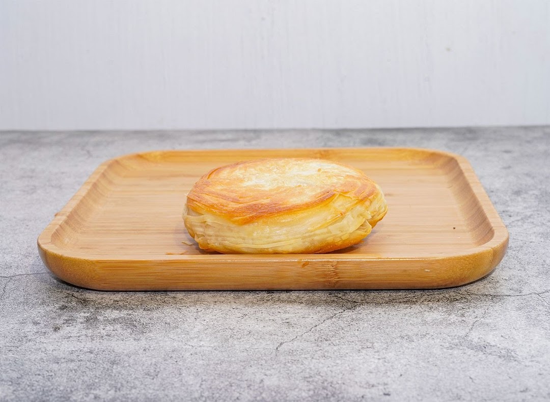 A golden-brown, flaky pastry, possibly a rougamo, rests on a wooden serving tray.