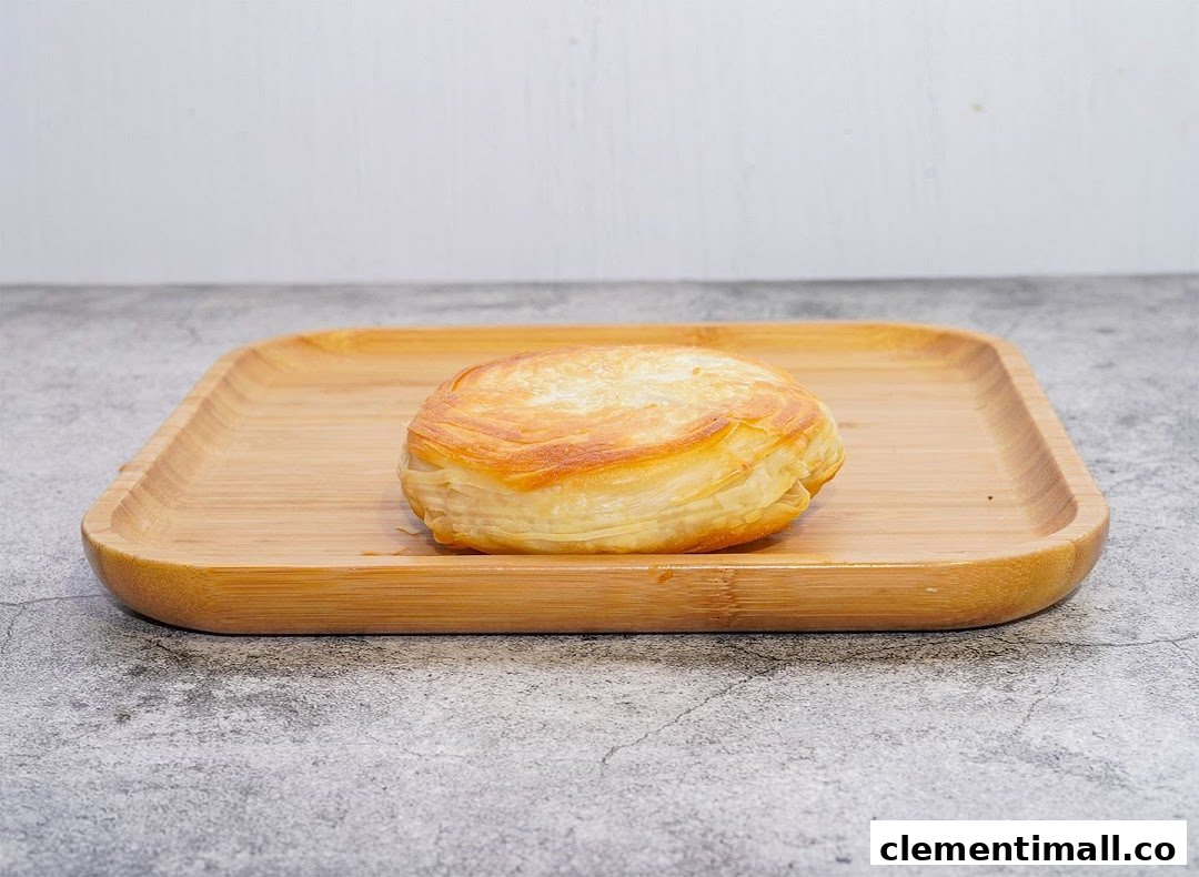 A golden-brown, flaky pastry, possibly a rougamo, rests on a wooden serving tray.