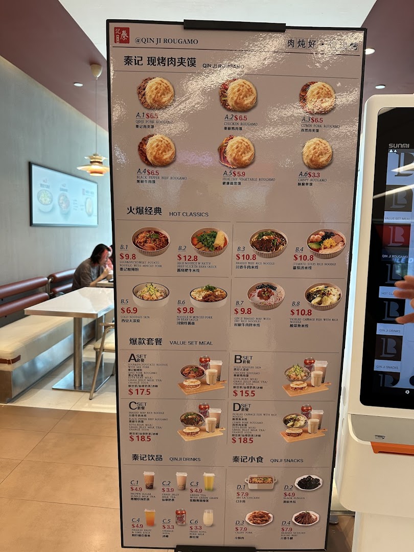 A large digital menu board at Qin Ji Rougamo displaying various rougamou, classic dishes, set meals, and drinks.