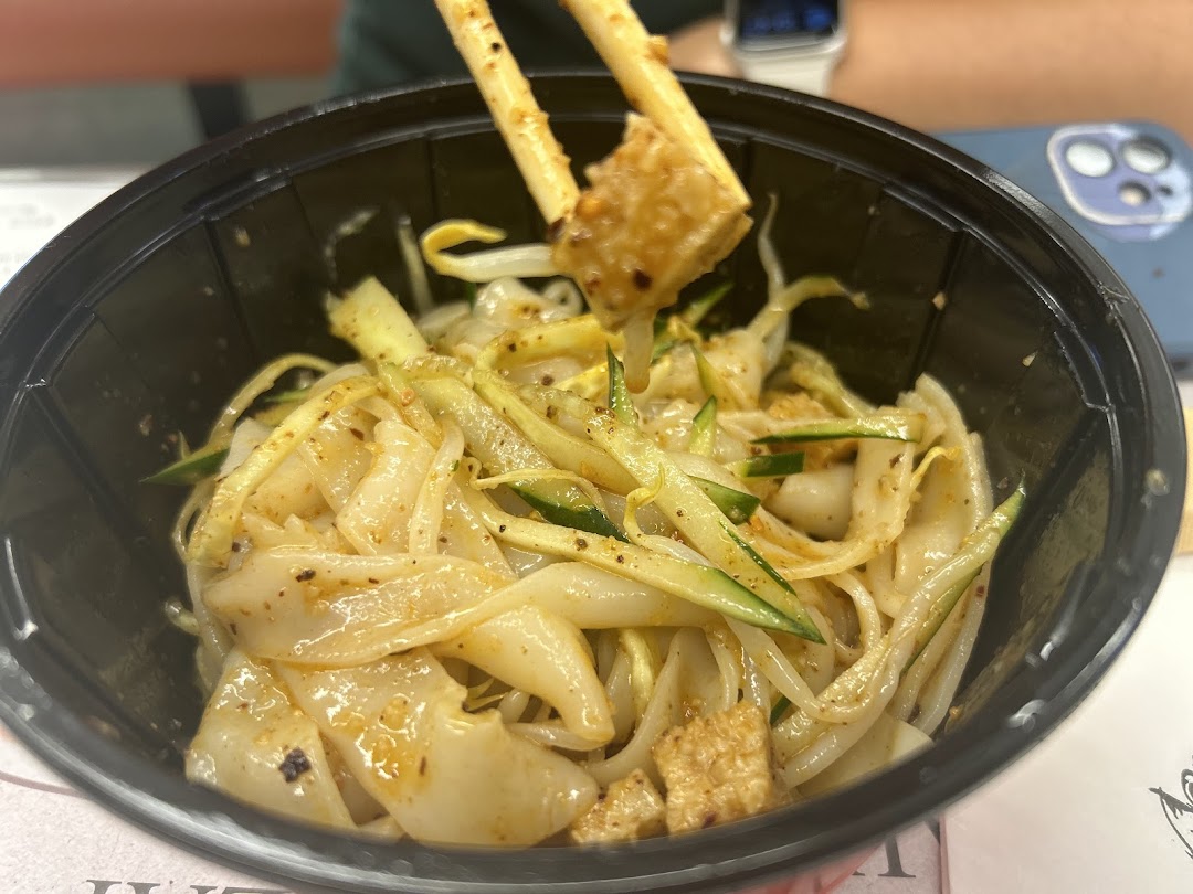 A close-up of a delicious noodle dish with cucumber and tofu, being enjoyed with chopsticks.