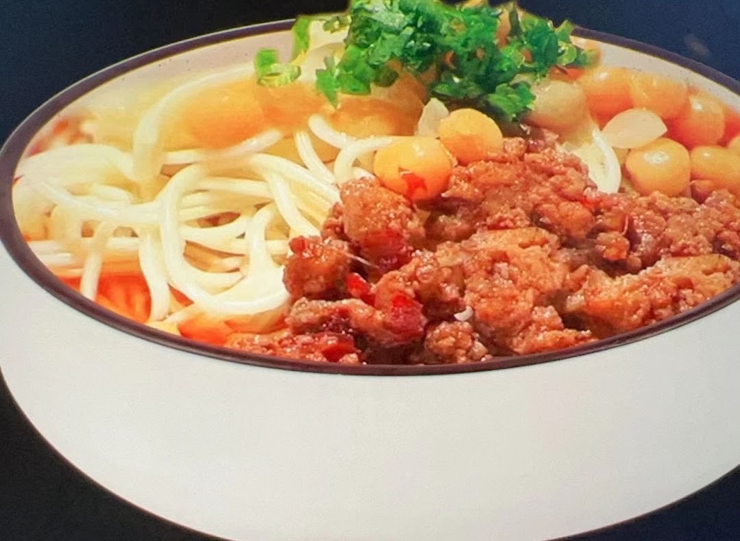 A close-up of a delicious bowl of noodles with minced meat, garnished with fresh herbs.