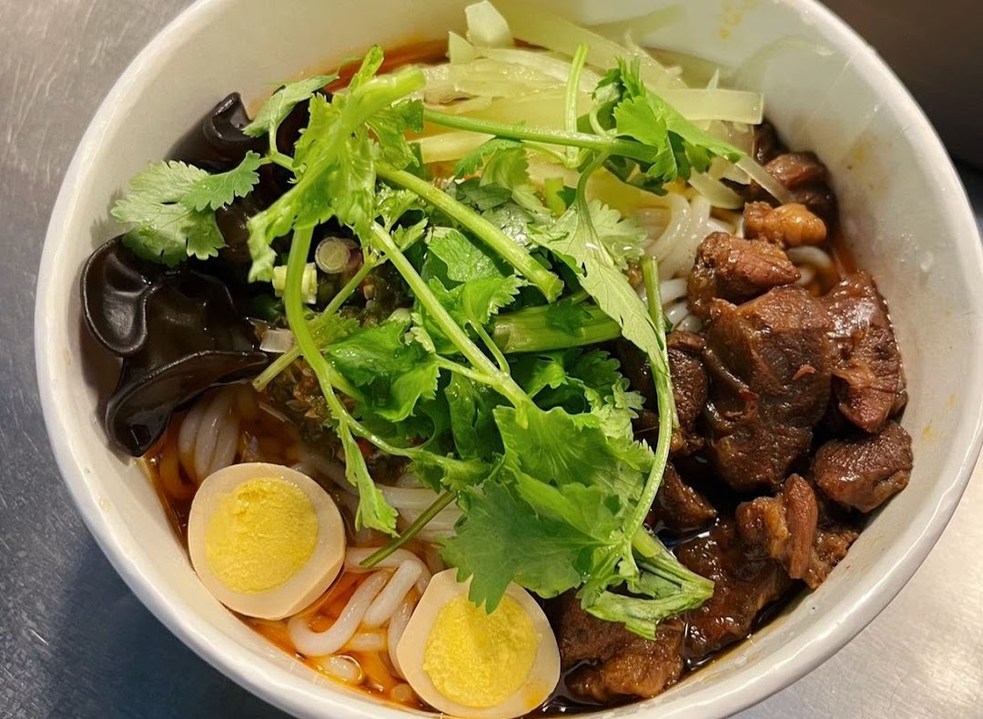 A close-up of a delicious bowl of noodles with braised meat, quail eggs, wood ear mushrooms, and fresh cilantro.