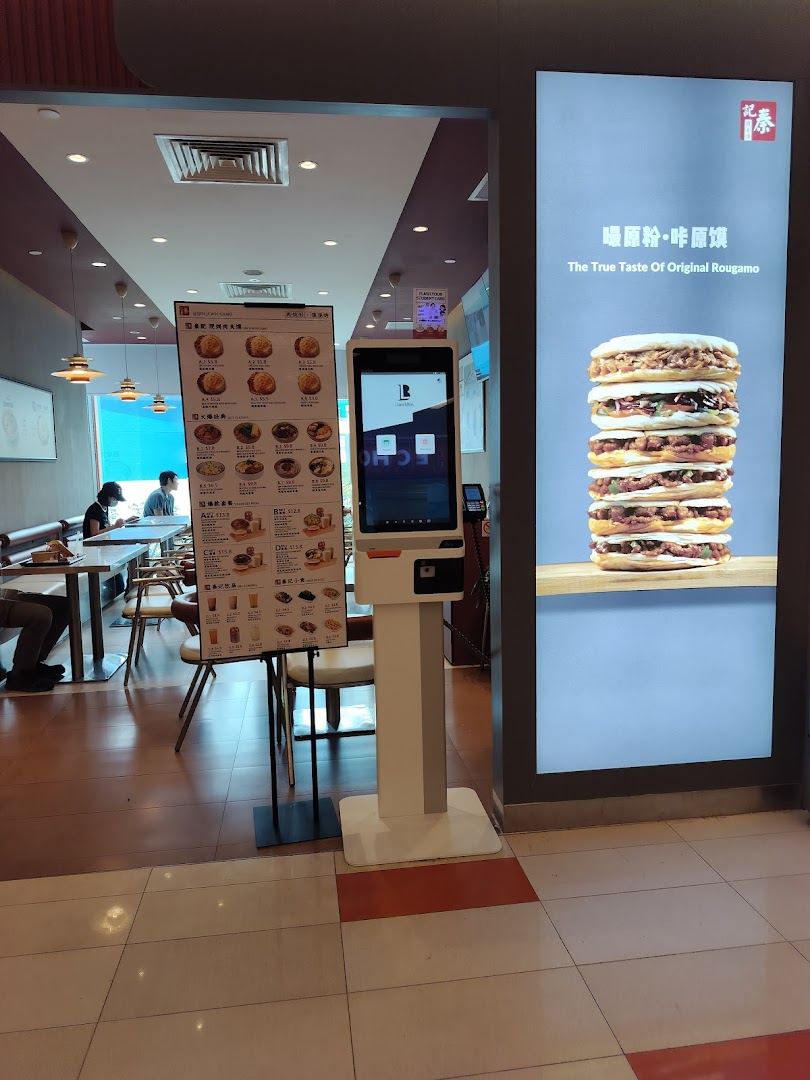 View of Qin Ji Rougamo's entrance, featuring a self-service kiosk, menu stand, and a large food display.