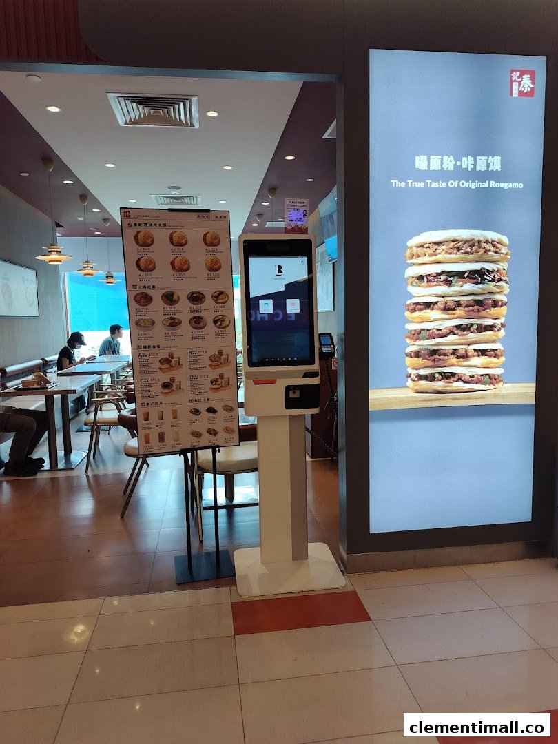 View of Qin Ji Rougamo's entrance, featuring a self-service kiosk, menu stand, and a large food display.