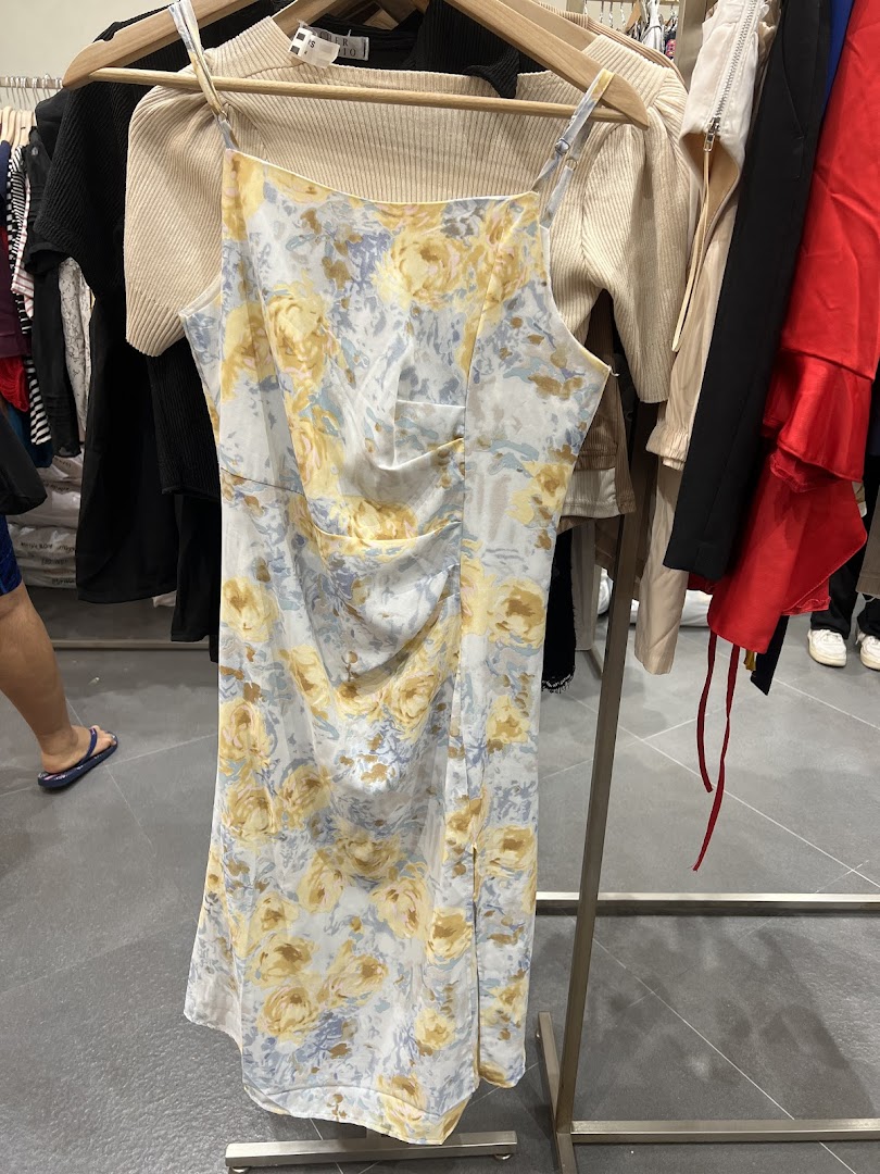 A beautiful floral dress with yellow and blue patterns hangs on a rack inside a clothing store.