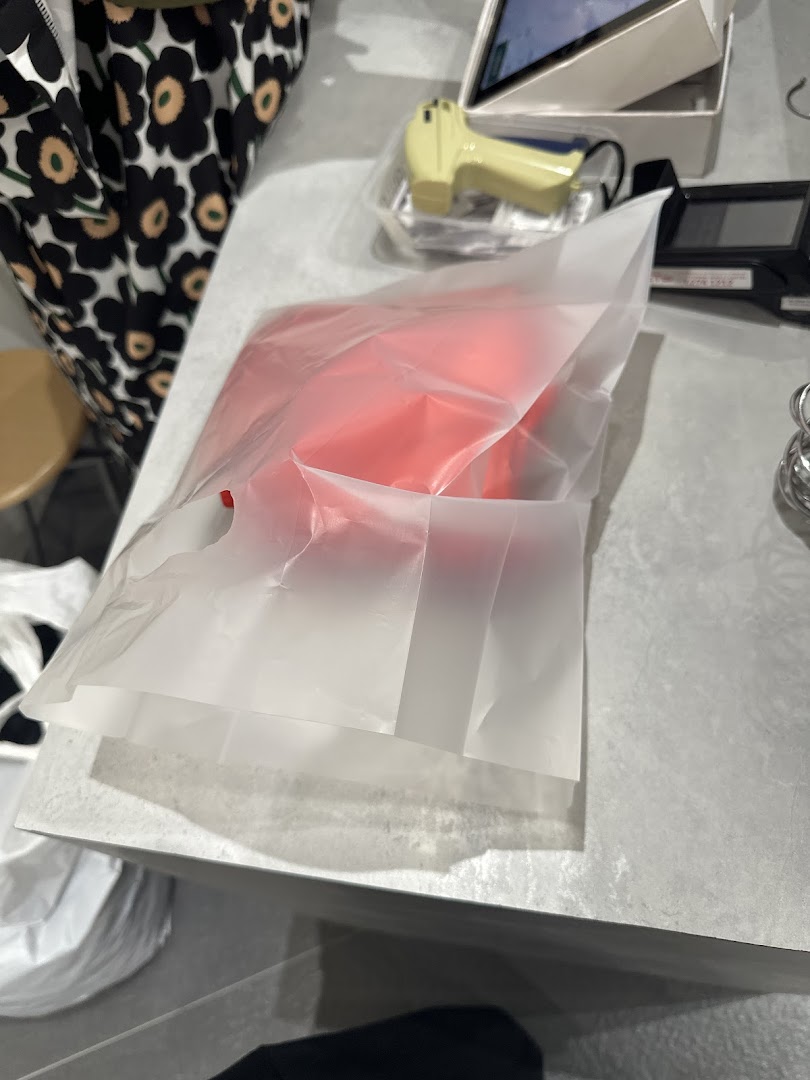 A red item in a translucent shopping bag on a counter, likely after a purchase.