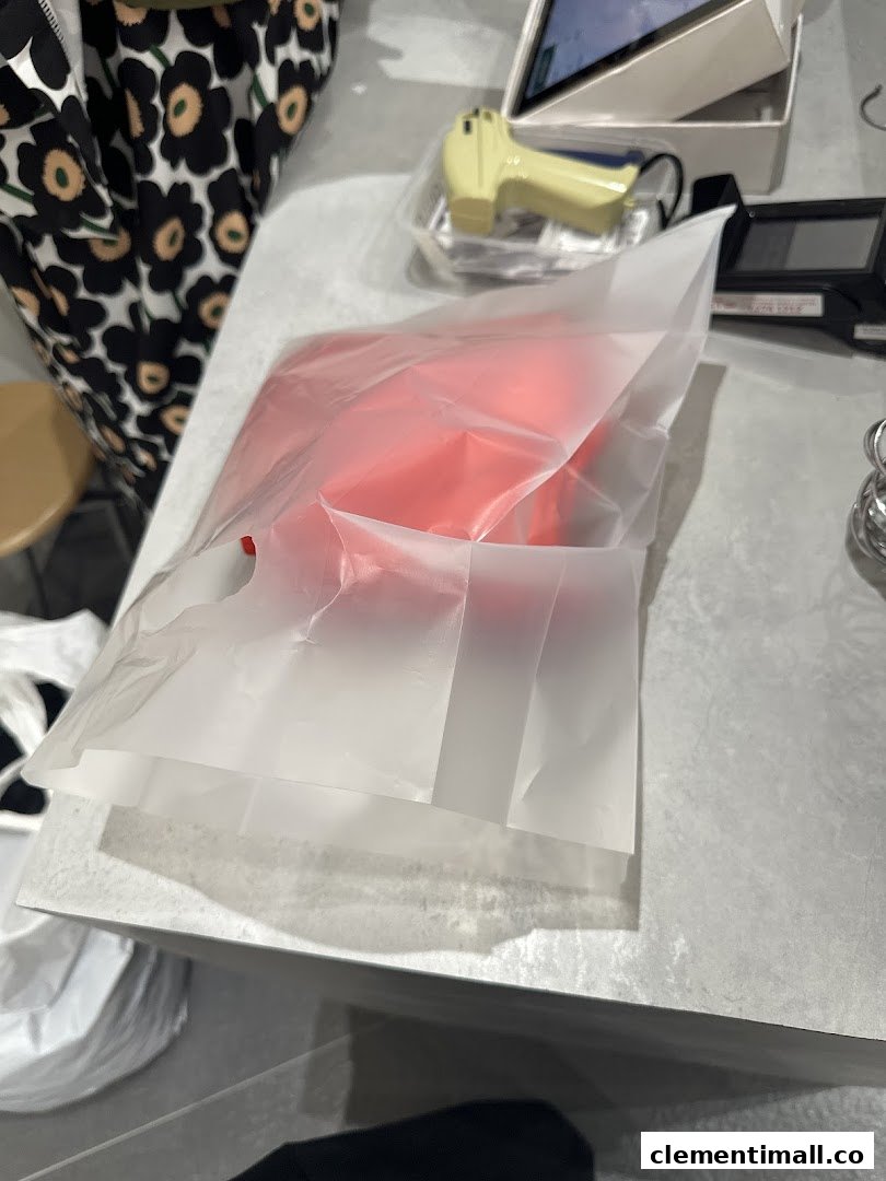 A red item in a translucent shopping bag on a counter, likely after a purchase.