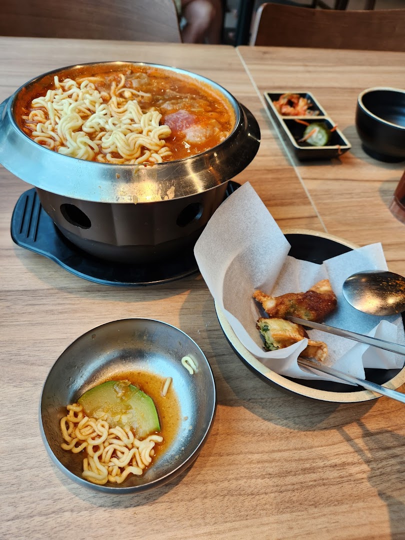 A bubbling Korean hot pot with ramen noodles, accompanied by fried dumplings and traditional side dishes.