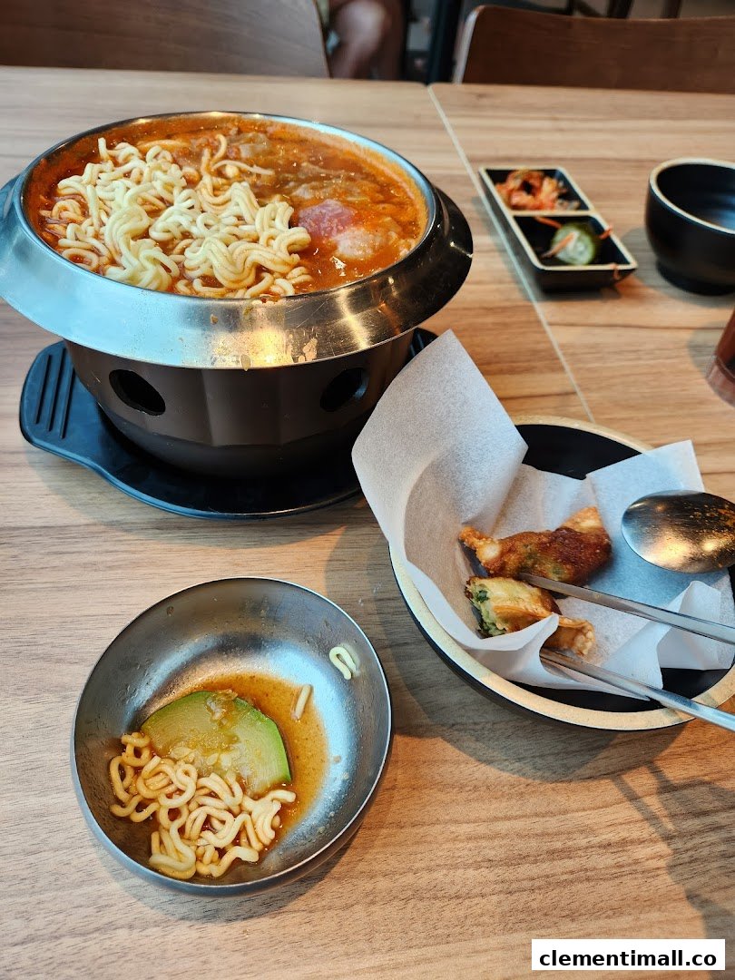 A bubbling Korean hot pot with ramen noodles, accompanied by fried dumplings and traditional side dishes.