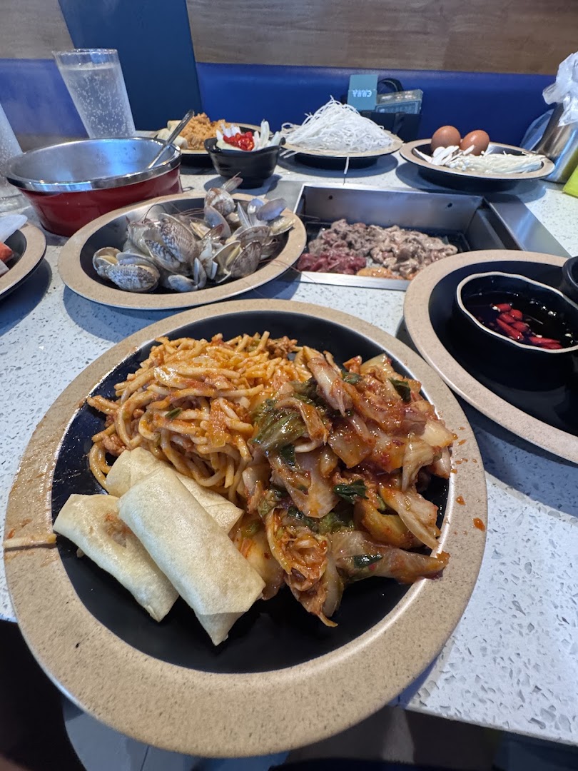 A vibrant table spread at Seoul Garden featuring hotpot ingredients, noodles, kimchi, and spring rolls.
