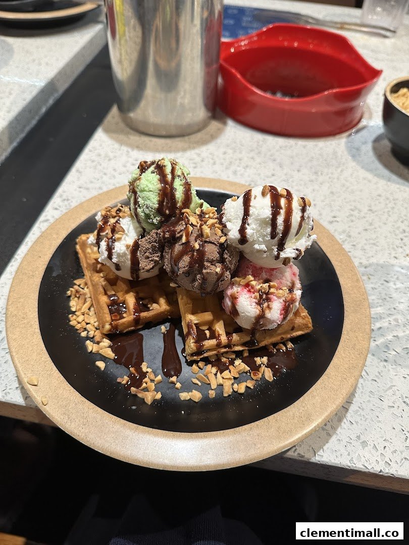 Waffles topped with multiple scoops of ice cream, chocolate sauce, and nuts on a black plate.