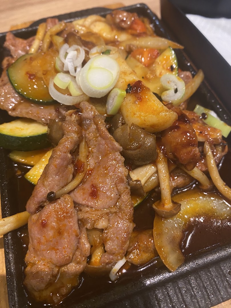 A close-up of a sizzling plate featuring tender meat, fresh vegetables, and mushrooms.