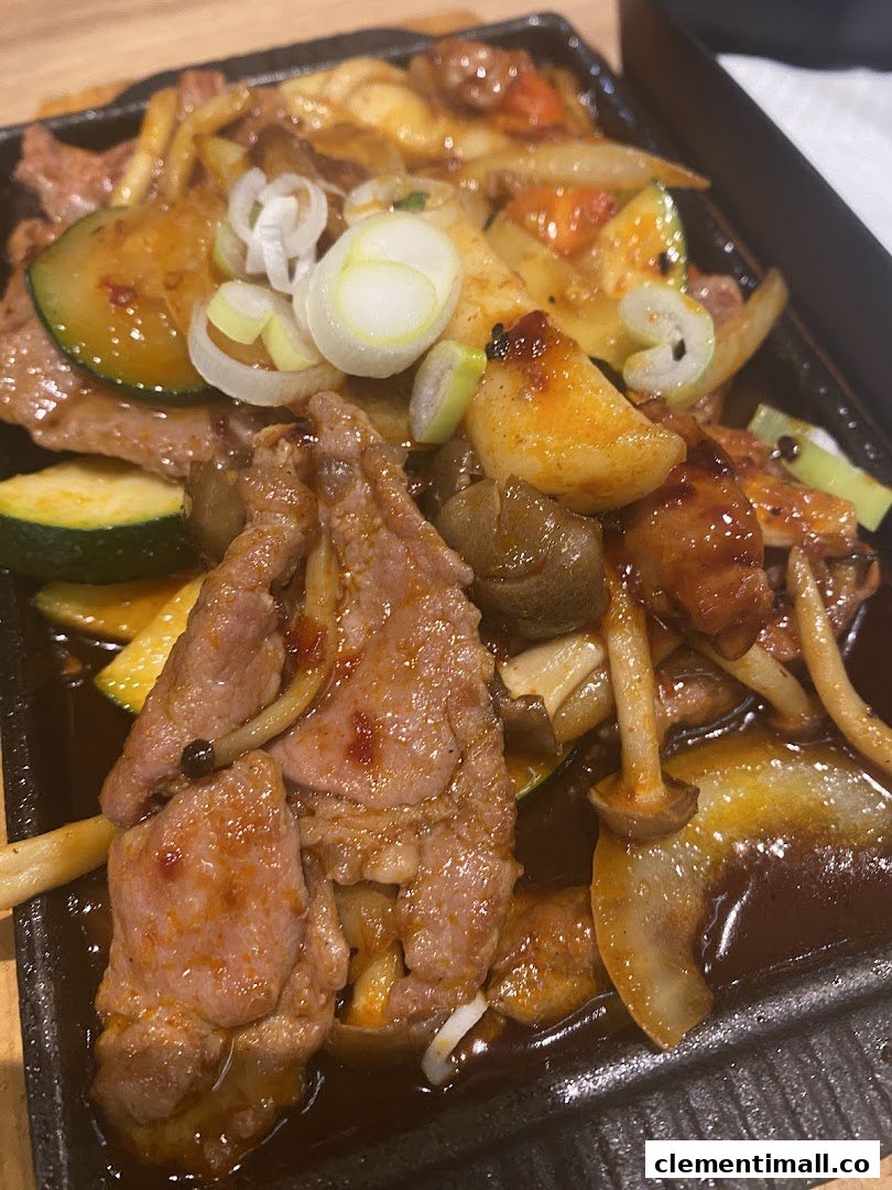 A close-up of a sizzling plate featuring tender meat, fresh vegetables, and mushrooms.