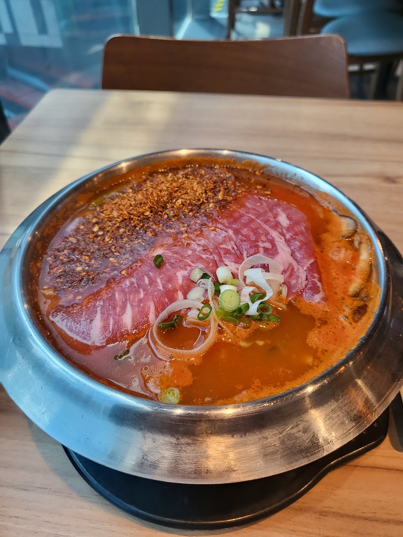 A vibrant hotpot dish with raw beef slices, chili flakes, and spring onions in a simmering broth.
