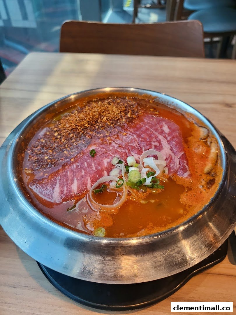 A vibrant hotpot dish with raw beef slices, chili flakes, and spring onions in a simmering broth.