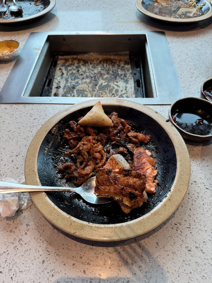 A plate of grilled meat and salmon with a samosa, next to a built-in table grill.