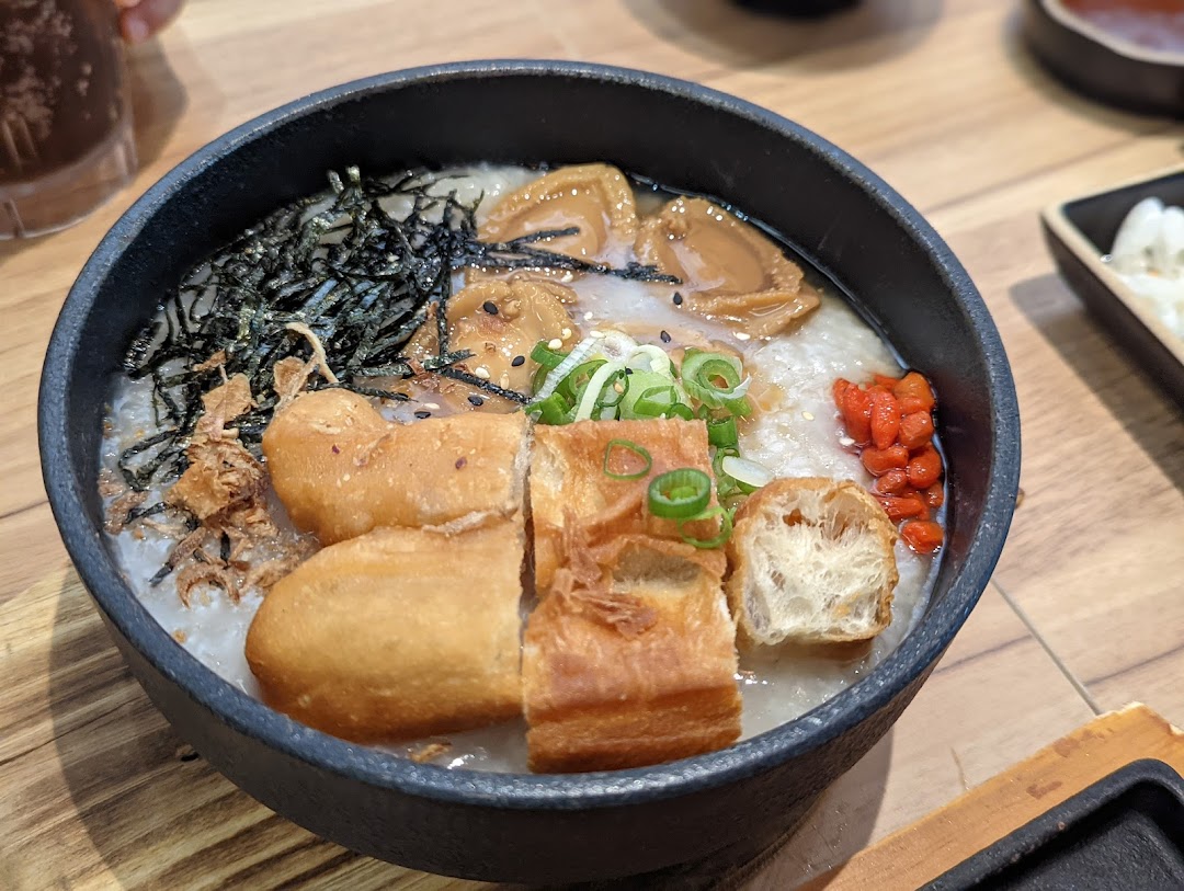 A close-up of a hearty bowl of congee with abalone, fried dough fritters, seaweed, and goji berries.