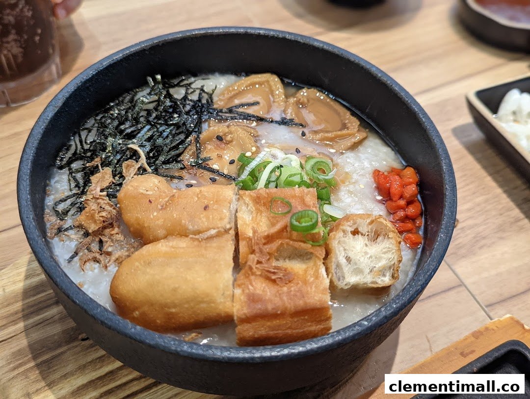 A close-up of a hearty bowl of congee with abalone, fried dough fritters, seaweed, and goji berries.