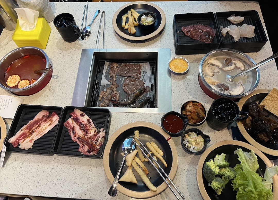 A vibrant table spread featuring Korean BBQ and hotpot with various ingredients and side dishes.