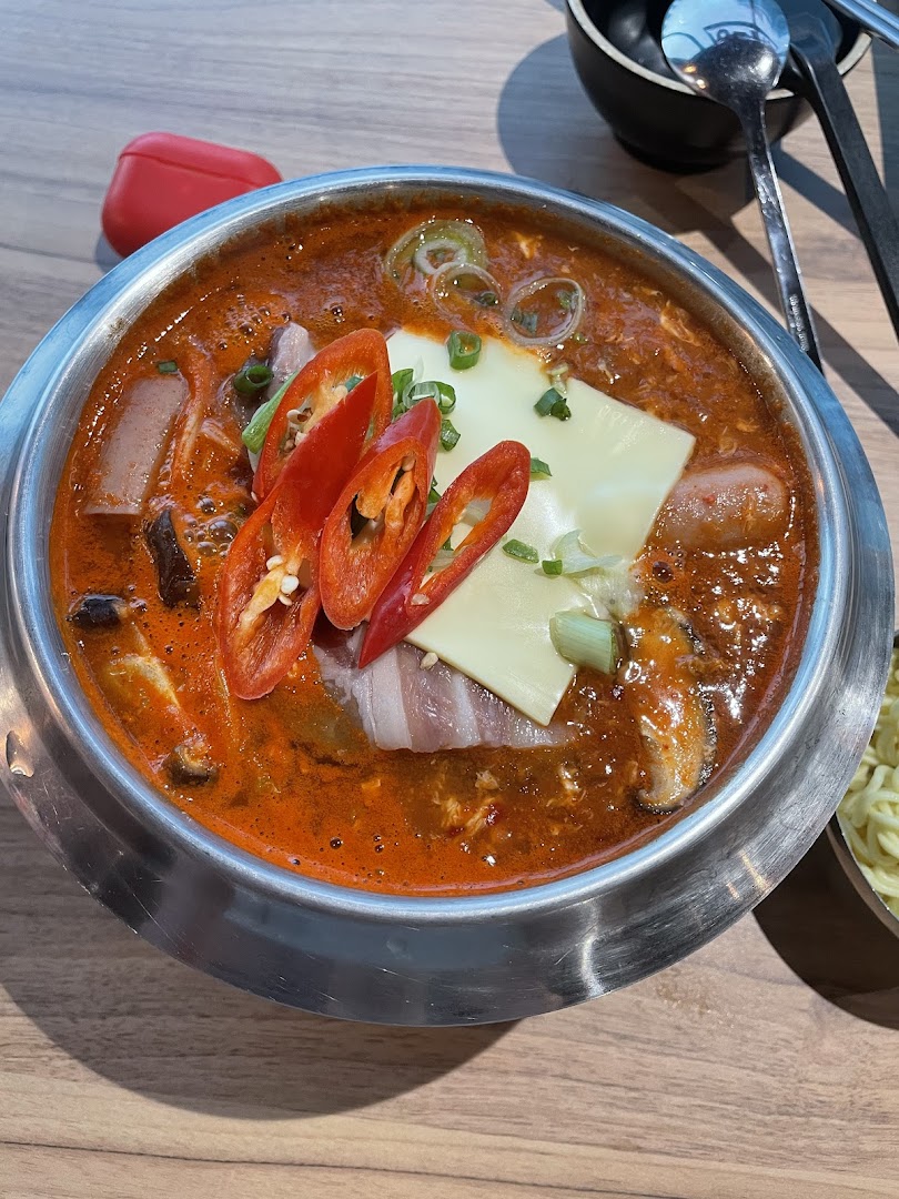 A vibrant Korean hotpot or stew with chili, cheese, and various ingredients in a metal pot.