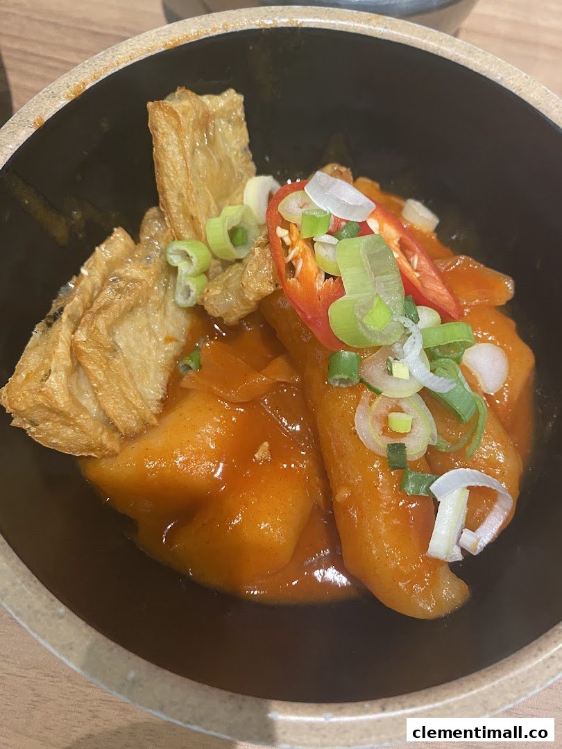 A close-up of a vibrant Korean dish with rice cakes, beancurd skin, chili, and spring onions in a rich sauce.