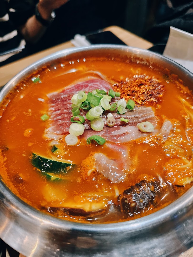A vibrant Korean hotpot with sliced beef, zucchini, and chili flakes, garnished with fresh spring onions.