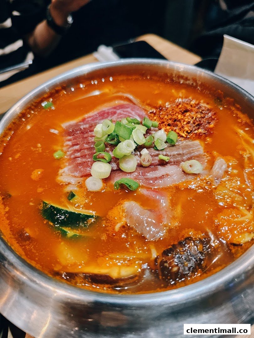 A vibrant Korean hotpot with sliced beef, zucchini, and chili flakes, garnished with fresh spring onions.