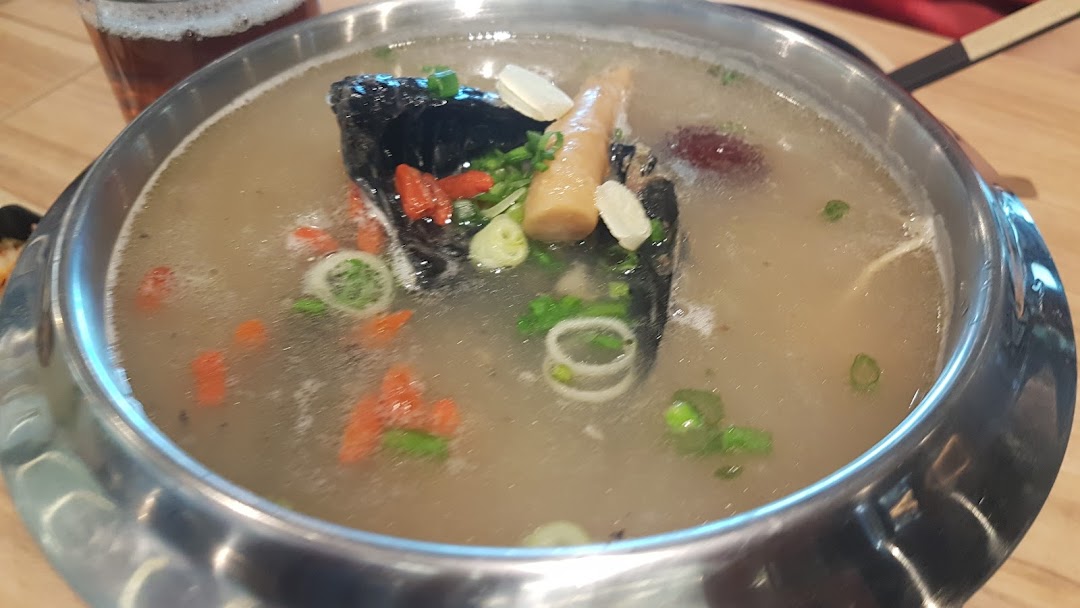 A close-up of a hearty Korean soup or hot pot dish, featuring dark meat, bamboo shoots, and goji berries.