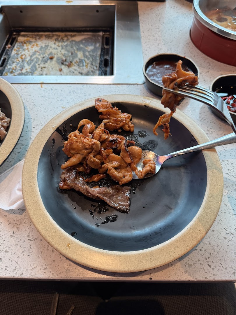 A plate of grilled meat and seafood with a fork, next to a built-in grill at Seoul Garden.
