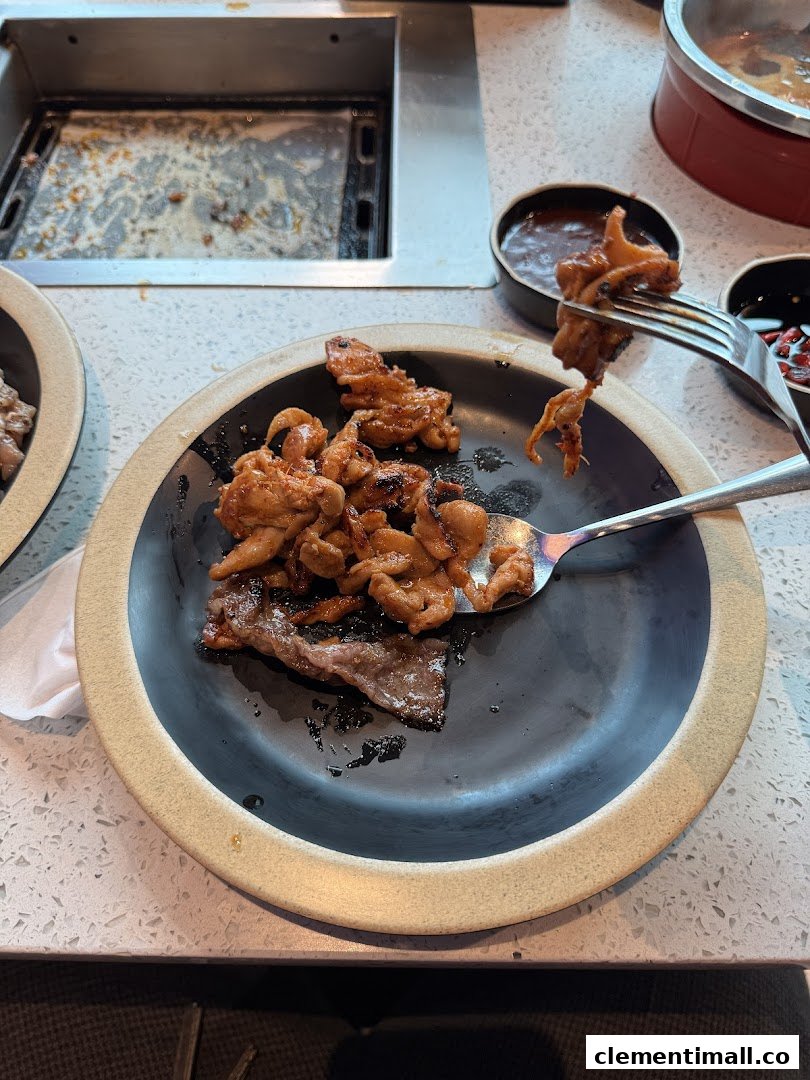 A plate of grilled meat and seafood with a fork, next to a built-in grill at Seoul Garden.
