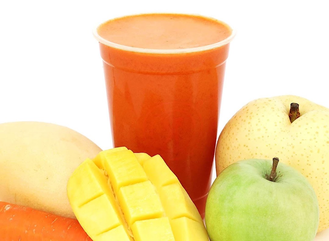 A vibrant cup of fresh juice surrounded by mango, carrot, apple, and pear on a white background.