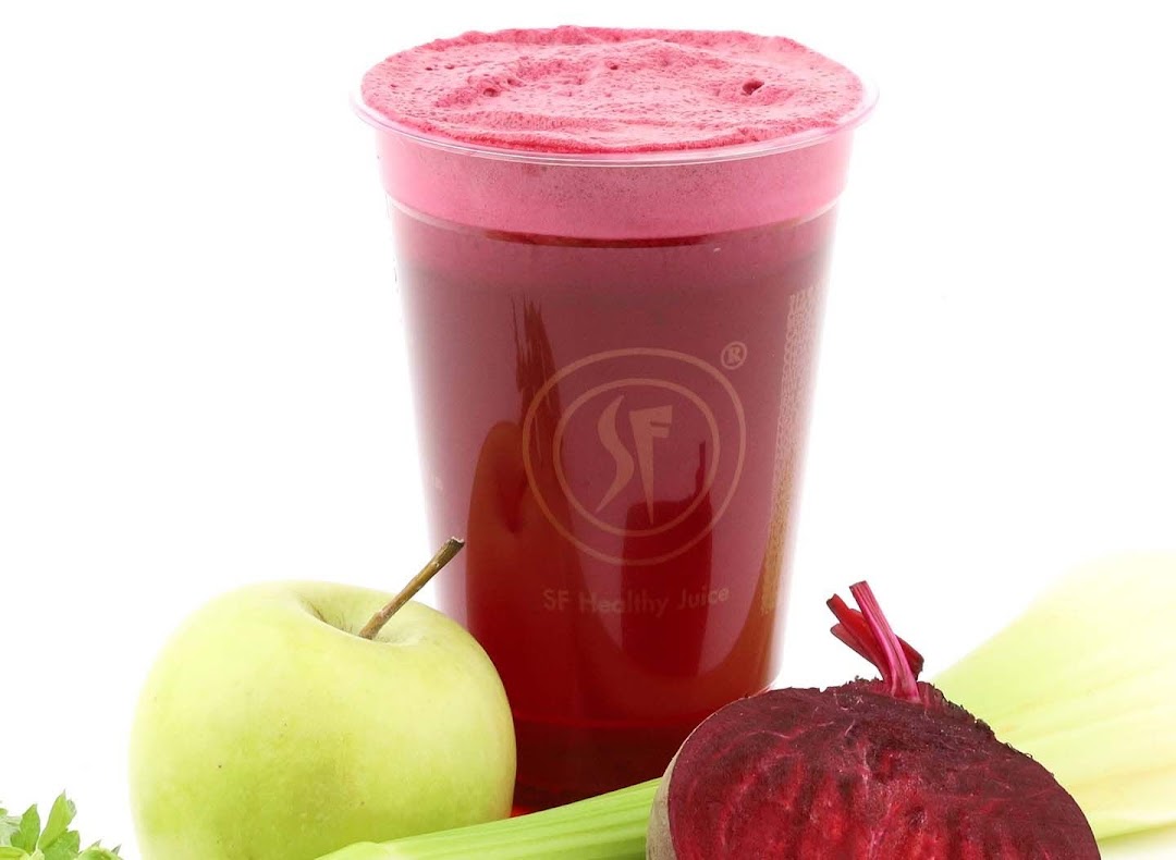 A vibrant red juice in a clear cup, surrounded by fresh apple, beetroot, and celery.