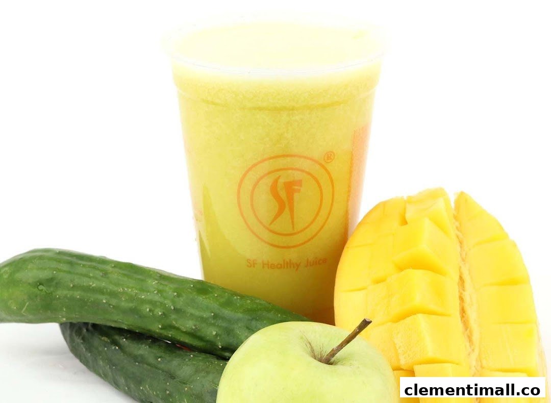A vibrant yellow juice in a branded cup, surrounded by fresh mango, cucumber, and green apple.