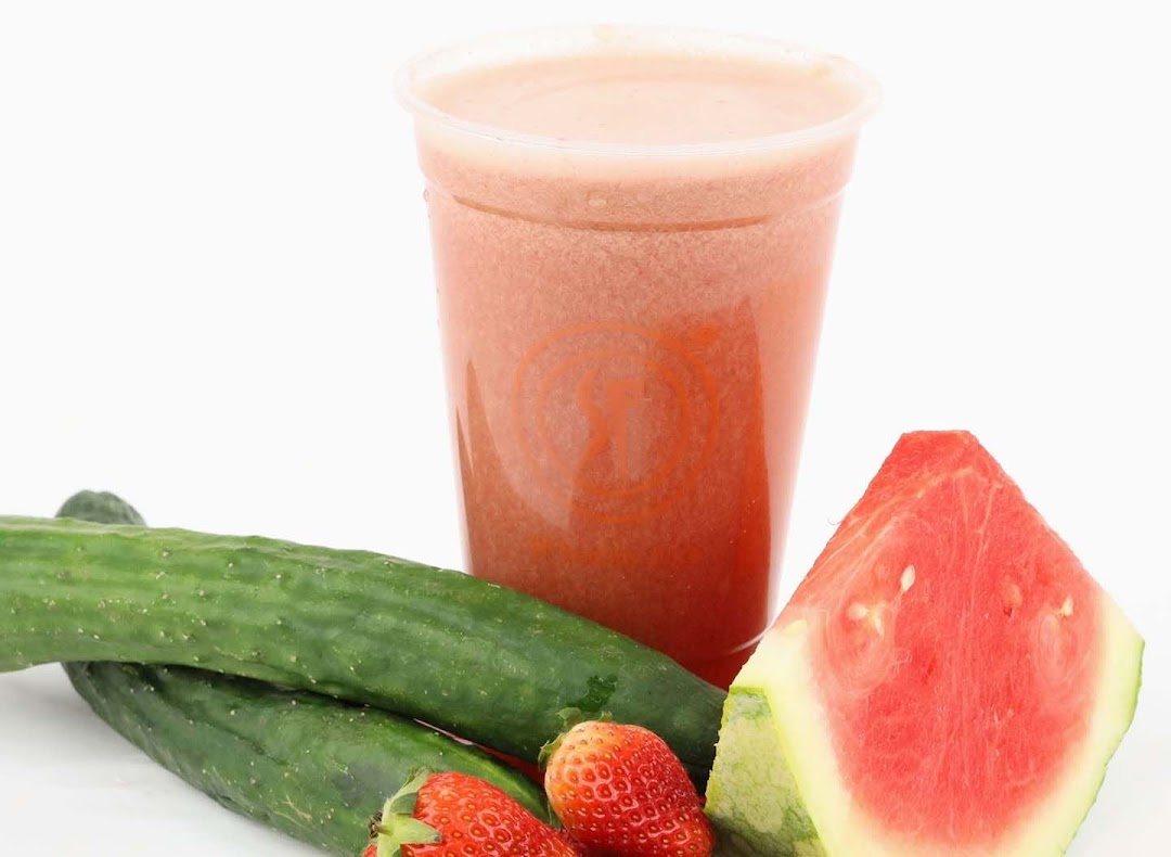 A refreshing fruit juice in a cup, surrounded by fresh watermelon, cucumbers, and strawberries.