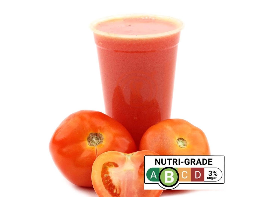 A vibrant tomato juice in a cup, surrounded by fresh tomatoes, with a Nutri-Grade B label.