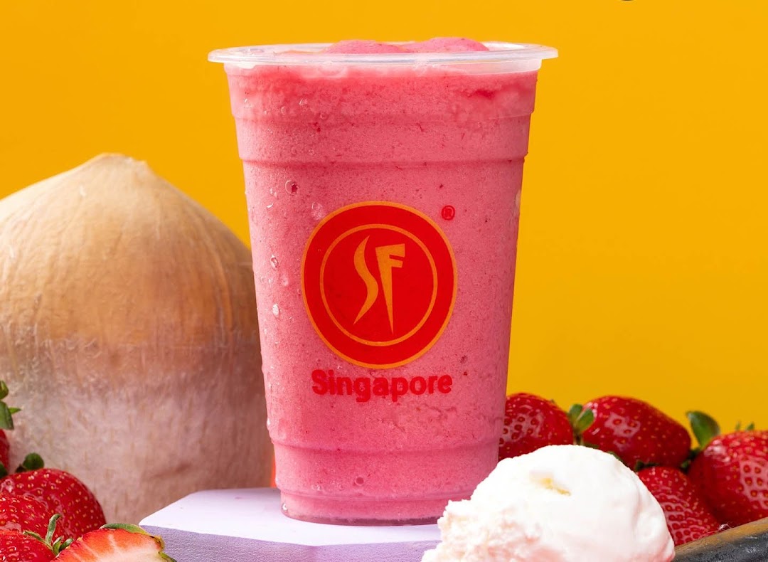 A vibrant pink fruit smoothie with strawberries, coconut, and ice cream against a yellow background.