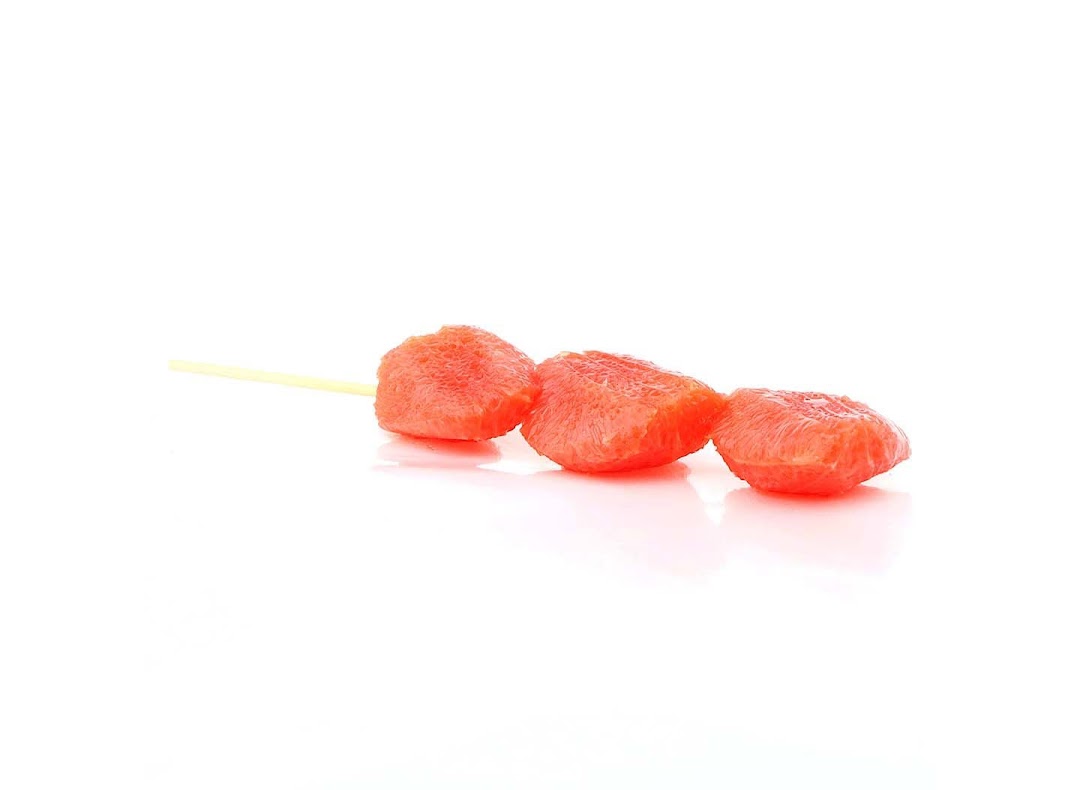 Three vibrant pink fruit segments on a skewer, presented on a clean white background.