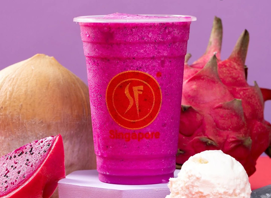A vibrant pink dragon fruit smoothie with fresh dragon fruit and coconut in the background.