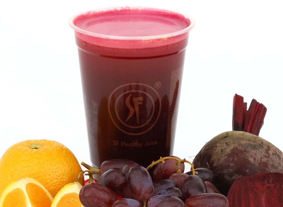 A vibrant red juice in a clear cup, surrounded by fresh oranges, grapes, and beetroot.