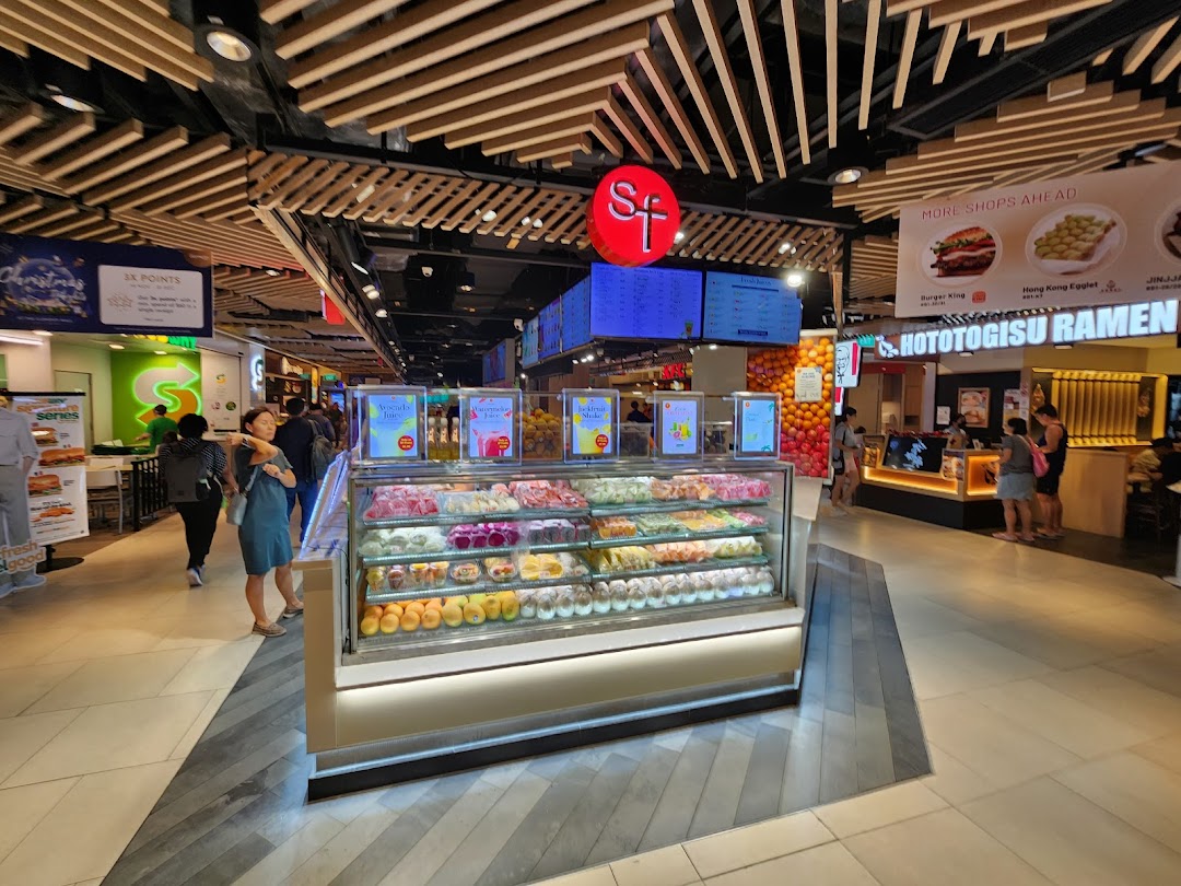 A vibrant fruit and juice stall, SF Fruits & Juices, with a colorful display of fresh produce and drinks in a bustling mall.
