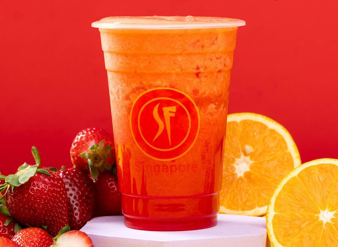 A vibrant fruit juice in a cup, surrounded by fresh strawberries and orange slices.