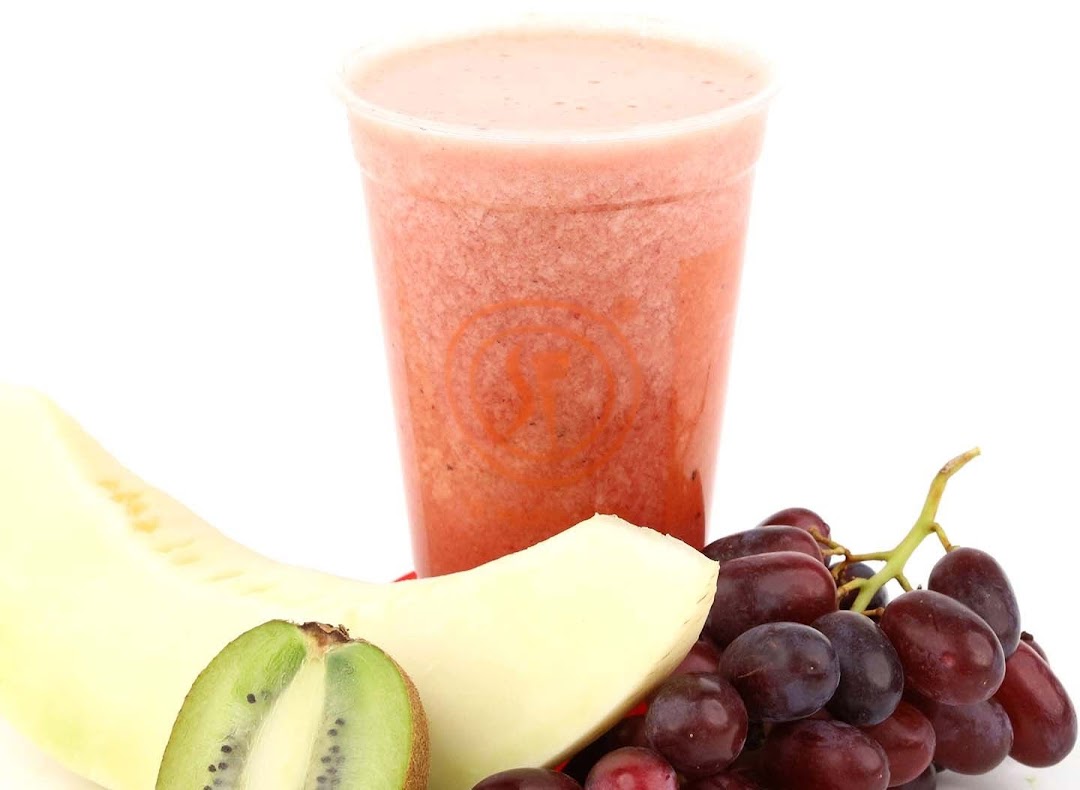 A vibrant fruit juice in a cup, surrounded by fresh kiwi, melon, and grapes.