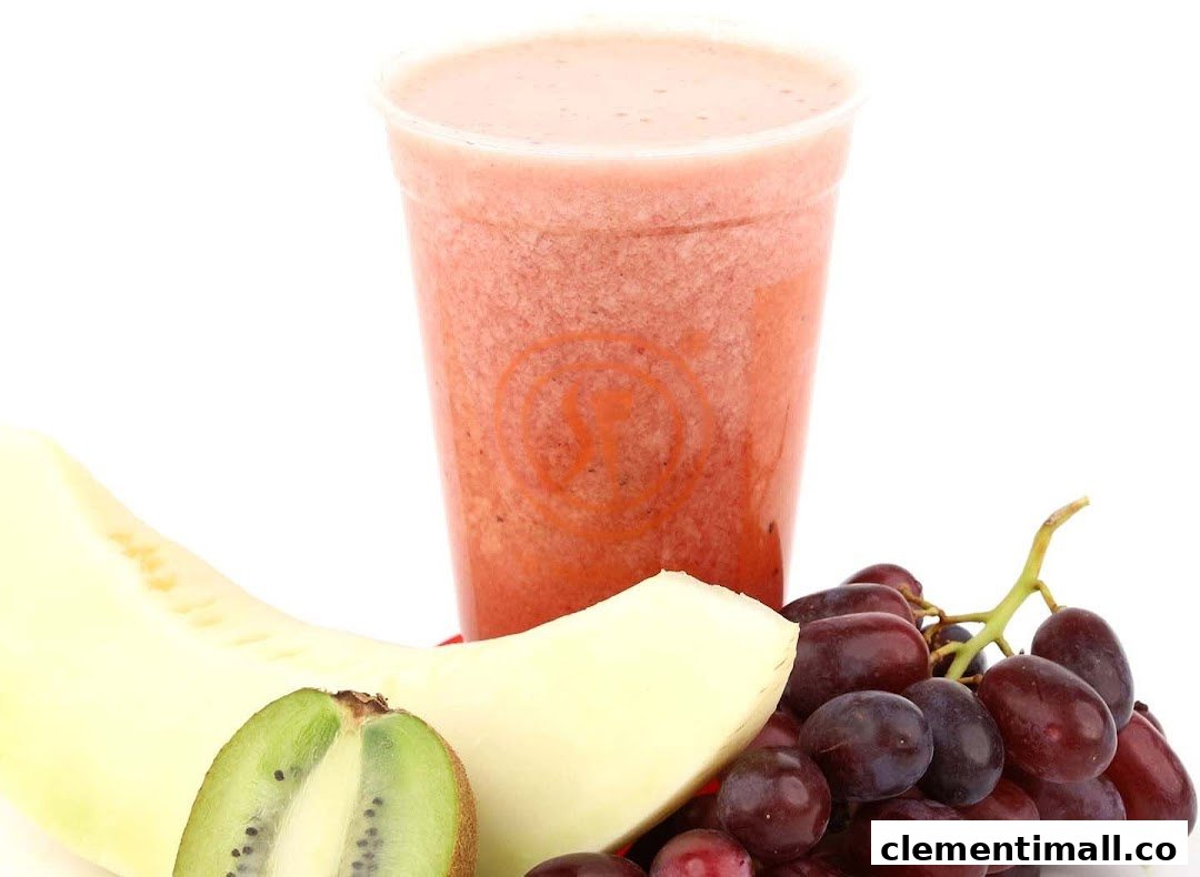 A vibrant fruit juice in a cup, surrounded by fresh kiwi, melon, and grapes.