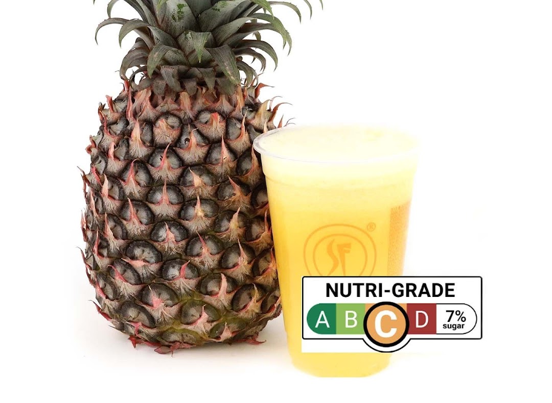 A fresh pineapple stands beside a cup of pineapple juice with a Nutri-Grade C label.