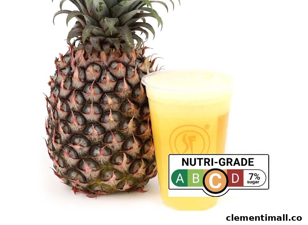 A fresh pineapple stands beside a cup of pineapple juice with a Nutri-Grade C label.
