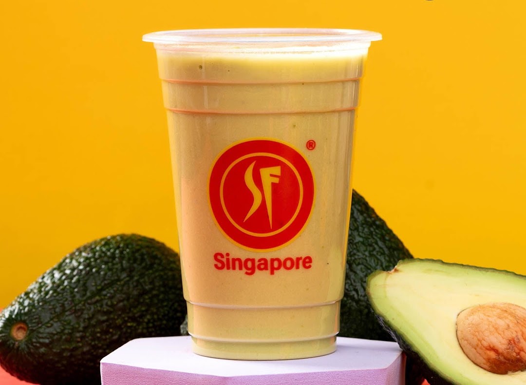 A creamy avocado smoothie in a clear cup, surrounded by fresh whole and halved avocados.