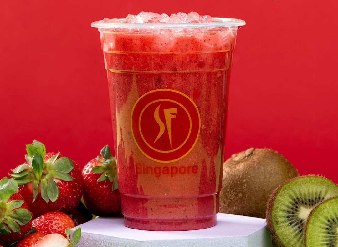 A vibrant strawberry smoothie with ice, surrounded by fresh strawberries and kiwi fruit.
