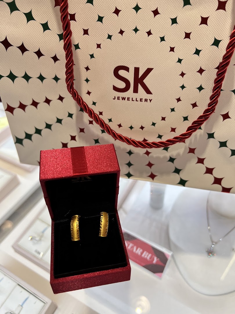 Elegant gold earrings in a red gift box, accompanied by an SK Jewellery shopping bag.